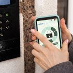 Young stylish woman getting access to the building by attaching smartphone to intercom. Concept of modern security technologies for access and smart home.