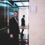 Stylish adult serious confident man in elegant suit standing in opened elevator of commercial building and looking away over shoulder